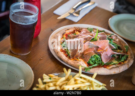 Close up di pizza servita sul vassoio in ceramica bianca con piastra in ceramica con forcella in acciaio inox e colazione coltello sulla tavola di legno, Nuova Zelanda. Foto Stock