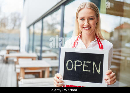 Giovane donna come una cameriera tenendo aperta la scheda di gesso nella parte anteriore del ristorante o bistrò Foto Stock