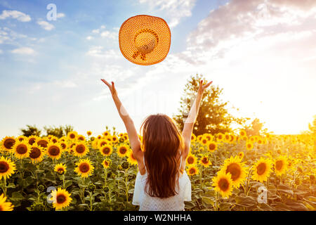 Giovane donna camminare in fiore campo di girasole gettando hat fino e divertirsi. Vacanze estive Foto Stock