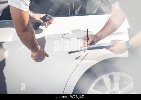 Contro lo sfondo di una vettura bianca, gli ispettori ispezionare il veicolo di trasporto, registrare difetti. Foto Stock