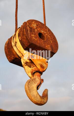 Chiusura di un gancio arrugginito sospeso di una grande gru con sfondo blu naturale Foto Stock