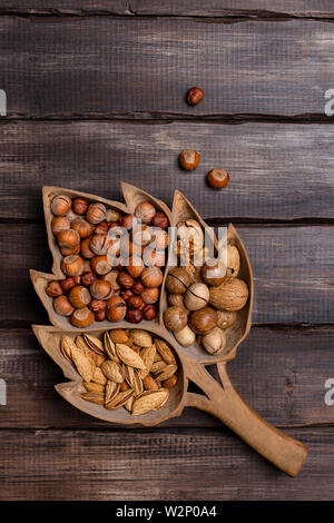 Varietà tipo dadi in background in legno. Le nocciole, le mandorle, le noci, le noci pecan nel vassoio in legno su legno scuro dello sfondo. Concetto di raccolto. Vista superiore, copia Foto Stock