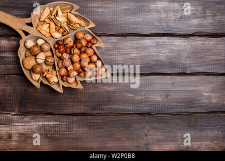 Varietà tipo dadi in background in legno. Le nocciole, le mandorle, le noci, le noci pecan nel vassoio in legno su legno scuro dello sfondo. Concetto di raccolto. Vista superiore, copia Foto Stock