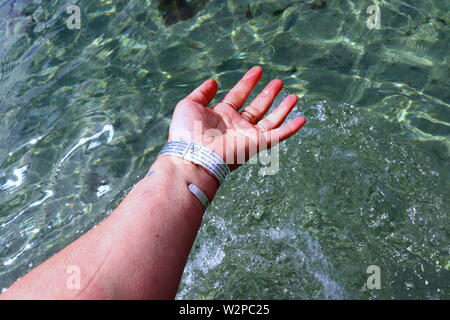 Donna di mano con argento braccialetti e anelli, spruzzi di acqua oceanica Foto Stock