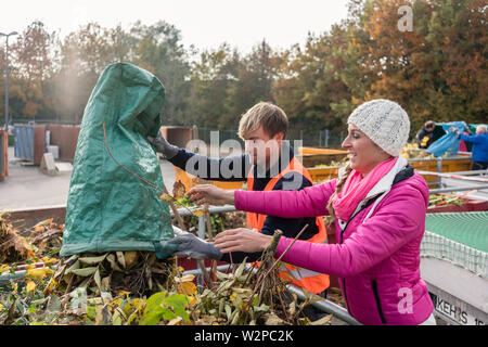 Donna e uomo dando verde dei rifiuti nel contenitore al centro di riciclaggio Foto Stock