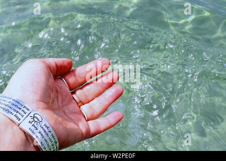 Donna di mano con argento braccialetti e anelli, spruzzi di acqua oceanica Foto Stock