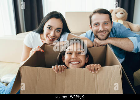 Incantevole piccola ragazza seduta in scatole di cartone , giocando con il suo genitore mentre si spostano nella nuova casa Foto Stock