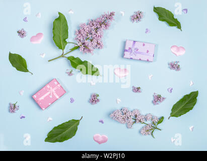 Ramoscelli, fiori e foglie di lilla, confezioni regalo e cuori tessili su sfondo blu. Foto Stock