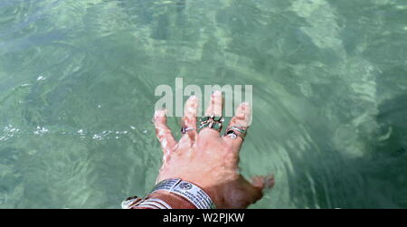 Donna di mano con argento braccialetti e anelli, spruzzi di acqua oceanica Foto Stock