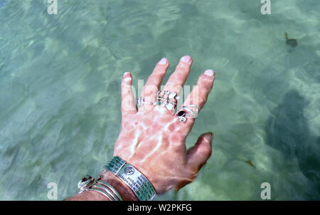 Donna di mano con argento braccialetti e anelli, spruzzi di acqua oceanica Foto Stock