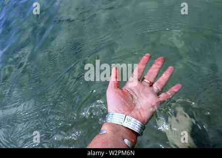 Donna di mano con argento braccialetti e anelli, spruzzi di acqua oceanica Foto Stock