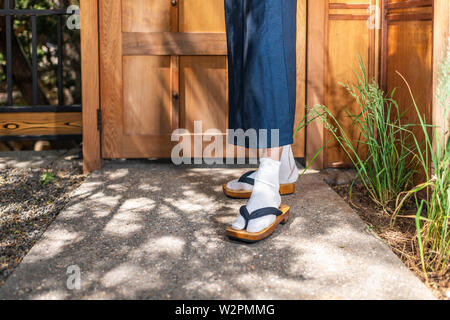 Piedi di uomo in kimono costume e geta dei tabi calzini scarpe nel giardino esterno in Giappone dal legno moderno porta contemporaneo Foto Stock