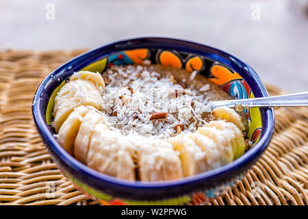 Primo piano della tazza colorata con farinata di amaranto e fette di banana con cocco grattugiato e noci pecan tagliate a pezzi Foto Stock