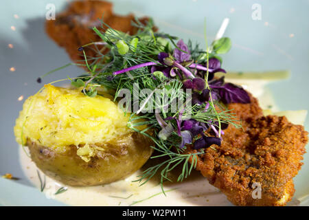 Un formaggio-guarnita di patate al forno servito con una fritta filetto di pesce in una camicia di pangrattato. Foto Stock