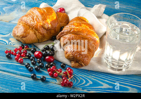 Ruddy freschi croissants con bacche giacciono su di un tavolo di legno accanto al fresco Ribes nero bacche, ribes rosso, ciliegie Foto Stock