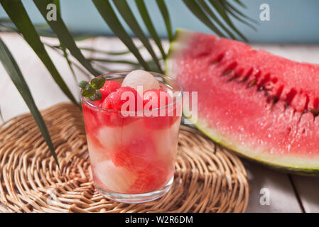 Macedonia di frutta con melone ed anguria sfere in vetro e pice di anguria sotto la foglia di palma sullo sfondo bianco Foto Stock