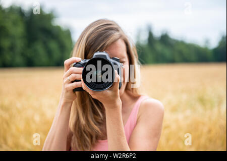 Vista frontale di una donna fotografa verso la fotocamera con la fotocamera reflex digitale in natura. Foto Stock