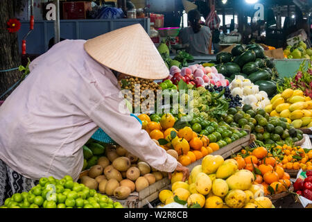 Produttore presso la sua frutta e verdura in stallo in un mercato di Hoi An, Vietnam. Foto Stock