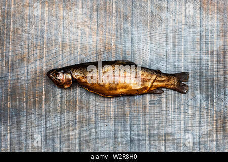 Angolo alto close up di uno appena affumicati trota intero su un tavolo di legno. Foto Stock