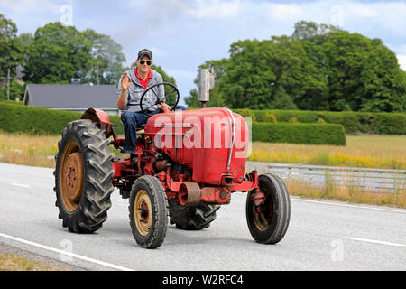 Kimito, Finlandia. Luglio 6, 2019. Giovane uomo saluta come egli unità classic Porsche-Diesel Super trattore su Kimito Tractorkavalkad, vintage parata del trattore. Foto Stock