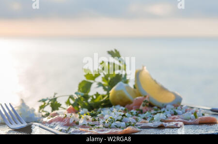 Filetti di salmone crudo, sedano, cipolla bianca e limone su un tavolo di pietra - Il mare sullo sfondo - Close-up Foto Stock