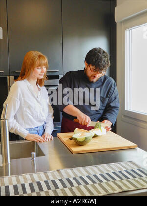 Redheaded girl orologi uno chef che tagliare il melone - Redheaded donna apprendista cuoco - Ritratto Foto Stock