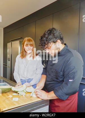 Due cuochi di taglio melone verde su una tavola di legno - Ragazza capelli rossi studente - fresco melone verde Foto Stock