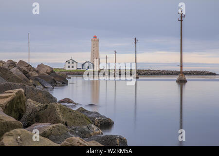 Faro e case disabitate in background. Alimentazione laterale piloni in acqua durante l'esposizione a lungo termine. La costa di pietra dell'isola di GRO Foto Stock