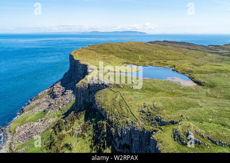 Fair Head big cliff e operazioni automatiche di fine campo all'angolo nord-est della Contea di Antrim, Irlanda del Nord, Regno Unito. Vista aerea con l'Oceano Atlantico e un lago. Foto Stock