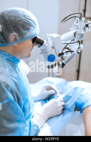 Oculista chirurgo guardando attraverso il microscopio chirurgico facendo operazione difficoltosa. Foto Stock