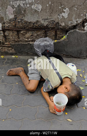 Bangkok, Tailandia - 23 dicembre 2010: un ragazzo giovane mendicante dormono sul ciglio della strada di thanon Rama 1 Foto Stock