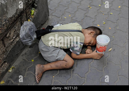 Bangkok, Tailandia - 23 dicembre 2010: un ragazzo giovane mendicante dormono sul ciglio della strada di thanon Rama 1 Foto Stock