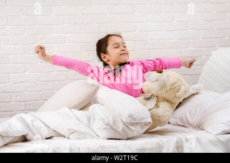 Grazioso fanciullo ragazza si risveglia dal sonno e sbadigli nel letto la mattina Foto Stock