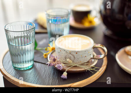 Diversi tipi di caffè in una tazza al buio su un tavolo, due bicchieri di acqua fredda e di fiori di primavera sulla tabella, vista dall'alto Foto Stock