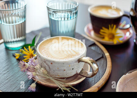 Diversi tipi di caffè in una tazza al buio su un tavolo, due bicchieri di acqua fredda e di fiori di primavera sulla tabella, vista dall'alto Foto Stock
