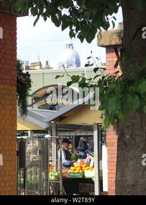 Foto guardando nella parte esterna bancarelle di frutta a Leeds City Market, con un uomo con una grande anguria a una pressione di stallo di frutta. Foto Stock