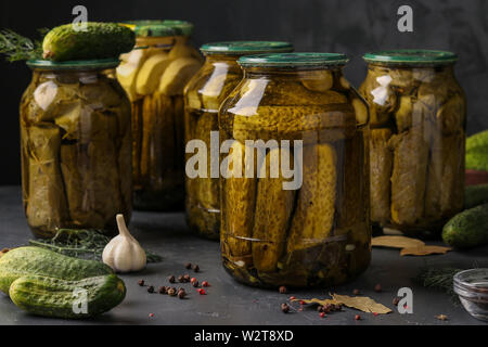 Diversi i cetrioli sottaceto con zucchine, aglio e foglie di uva in vasi su uno sfondo scuro, la foto in orizzontale Foto Stock