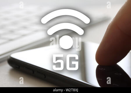 5G un concetto di rete con il dito toccando lo smartphone con lo schermo e la tastiera in background. Accesso wireless a internet simbolo nella parte anteriore del display. Foto Stock