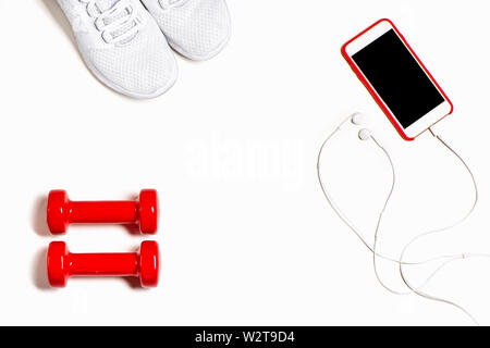 Piano di composizione dei laici con le scarpe da ginnastica, le cuffie, il telefono cellulare e il rosso manubri isolati su sfondo bianco. Vista dall'alto. Foto Stock