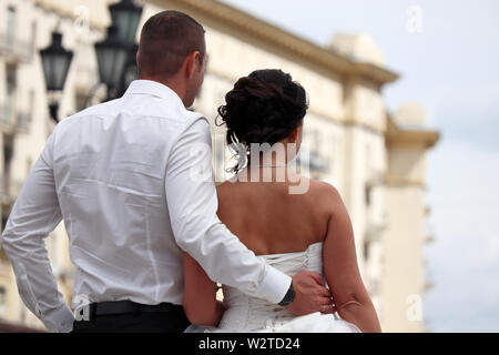 Nozze in una città, lo sposo abbraccia la vita della sposa, in vista posteriore Appena una coppia sposata, concetto di nuova famiglia guardando al futuro Foto Stock