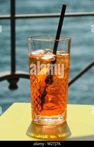 Vista ravvicinata di un bicchiere di Aperol Spritz su un tavolo con acqua in background. N. persone. Foto Stock