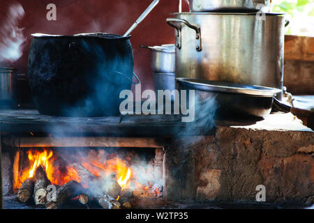 Vecchio stile di cottura con grande pentola a fuoco aperto. Nero ferro grande pentola di cottura tradizionale sul registro di fuoco di legno con visibile di fiamme e fumo. Foto Stock