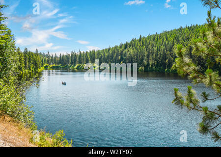 Un solitario piccola barca da pesca con due pescatori galleggia sul Lago di granito nelle montagne del nord Idaho in un assolato pomeriggio di estate. Foto Stock