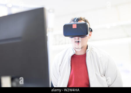 Giovane uomo che indossa cuffie per la realtà virtuale e che gestiva mentre si siede alla scrivania in un ufficio creativo Foto Stock