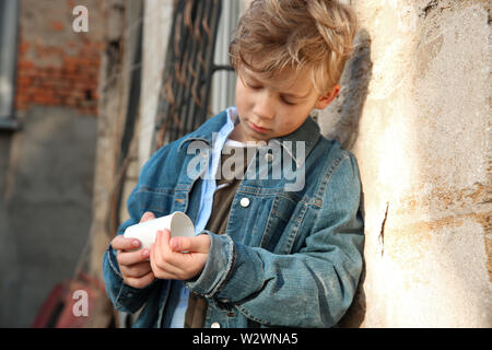 Senzatetto little boy conteggiare denaro all'aperto Foto Stock