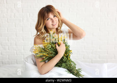 Bella giovane donna con bouquet di fiori di mimosa in camera da letto Foto Stock