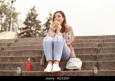 Bella giovane donna mangiare hamburger gustosi all'aperto Foto Stock