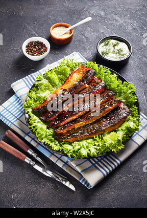 Arrosto di filetti di sgombro pesce servite con lattuga su una piastra nera su un concreto tavolo da cucina con salsa tartara in una ciotola, vista verticale da abov Foto Stock