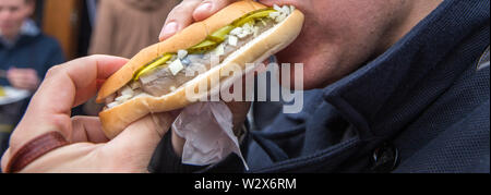 Uomo di mangiare su una strada hamburger di pesce con aringhe e cipolla e sottaceti Foto Stock