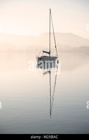 Bellissimo paesaggio unplugged immagine di yacht a vela seduto ancora nel lago calmo acqua nel distretto del lago durante la pacifica misty Autumn Fall sunrise Foto Stock